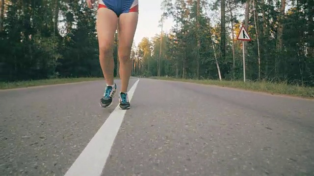 缓慢的运动。近距离观察一个面目全非的女人在一条路上跑过树林视频素材