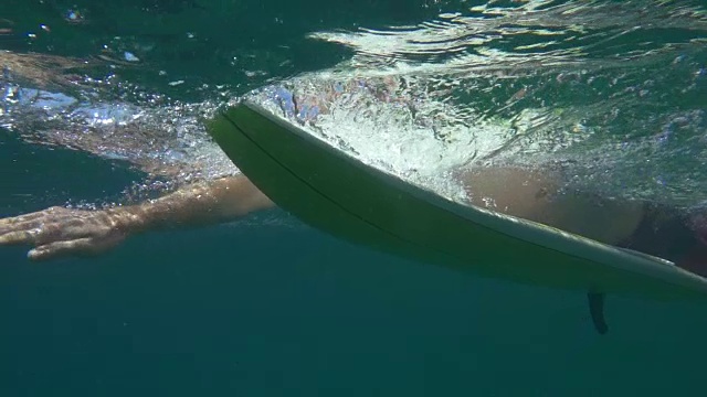 水下慢动作:一名面目全非的男性冲浪者在冲浪板上划水视频素材