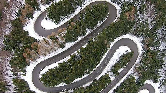 俯瞰一辆汽车驶过许多弯弯曲曲的壮观的高山垭口公路，在冬天的时候，穿过冷杉森林的景色视频素材