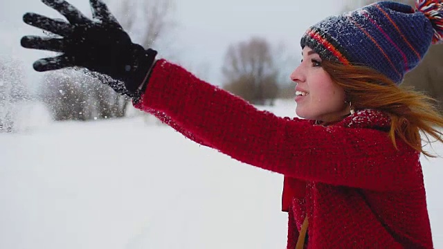 年轻的红发女子在户外享受降雪，笑着看着镜头，慢动作120帧/秒视频素材