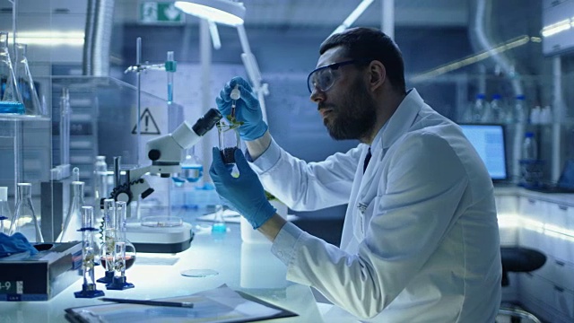 在现代实验室研究中，科学家用有机材料进行实验。他用吸管把肥料滴进装有植物的试管中。视频素材画面3