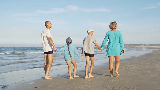 快乐的年轻家庭沿着海滩散步视频素材画面1