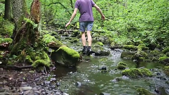 年轻男子在绿色森林里穿过一条小溪的特写视频素材