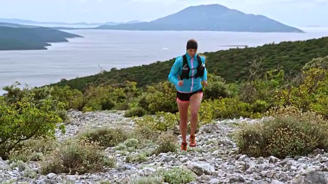 女运动员在一条小路上跑上山，山下有美丽的海景视频素材