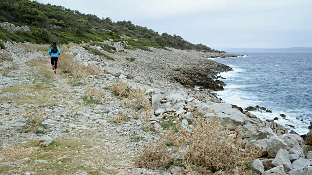 一个女人在一个阴天沿着海岸线的岩石小道上跑步视频素材