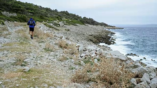 男性跑步者在恶劣天气下沿着岩石海滩跑步视频素材