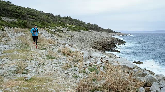 女跑步者在恶劣的天气下在海边的岩石小径上跑步视频素材