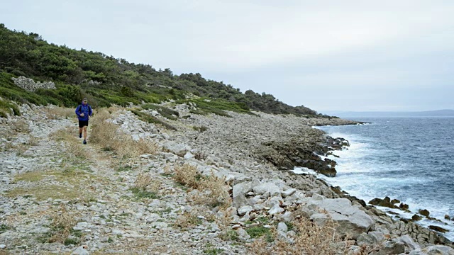 一个人在一个阴天沿着海岸线的岩石小道上跑步视频素材