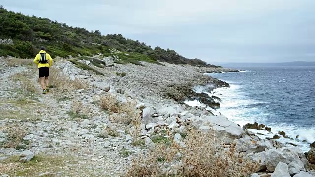 一个人在阴天沿着布满岩石的野生海岸线奔跑视频素材