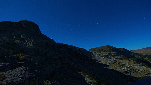 夜晚星星在山、湖和山峰上的时间流逝，移动的满月和阴影视频素材