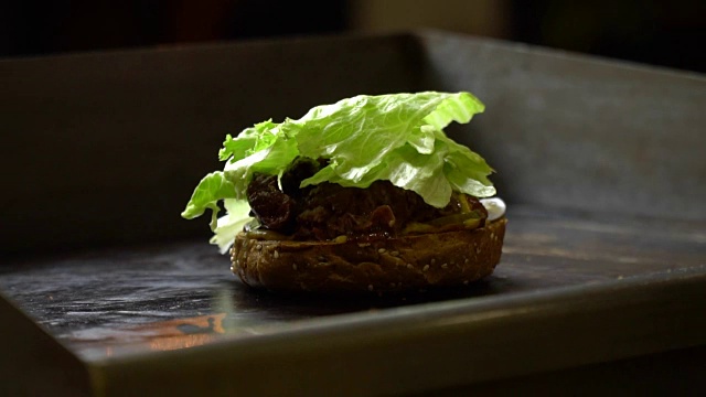 在一个开放的快餐厨房里烹饪汉堡的过程的特写。厨师在炉子上煎馒头。厨师把莴苣叶放进汉堡里。芝麻黑麦面包视频素材