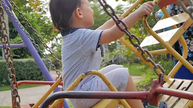 可爱的亚洲小男孩有乐趣的玩和骑在荡秋千在操场上的慢动作视频素材