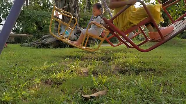 可爱的亚洲小男孩和女孩玩得很开心，在操场上一起骑秋千在日落时间在慢动作视频素材