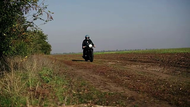 前面的观点，一个男人在一个乡村道路上骑摩托车黑色头盔和皮夹克。他正从照相机旁边经过视频素材