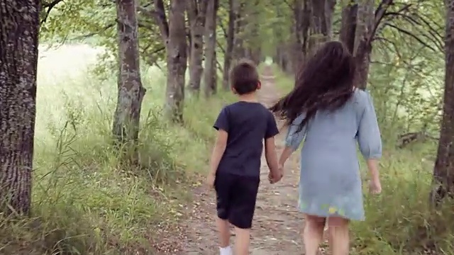 可爱快乐的小女孩和小男孩牵着手微笑着跑过森林。弟弟和妹妹一起散步视频素材