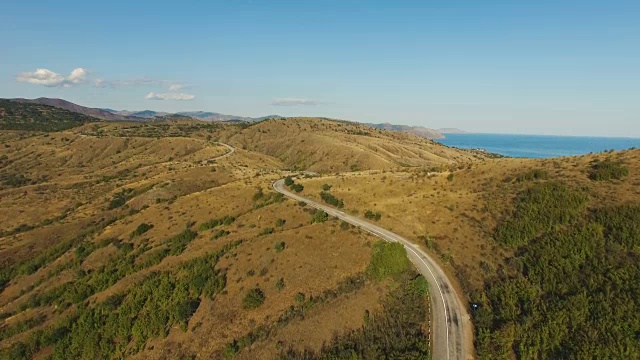 空中:高速公路穿过丘陵地带，有遥远的山脉和蓝色的海洋视频素材