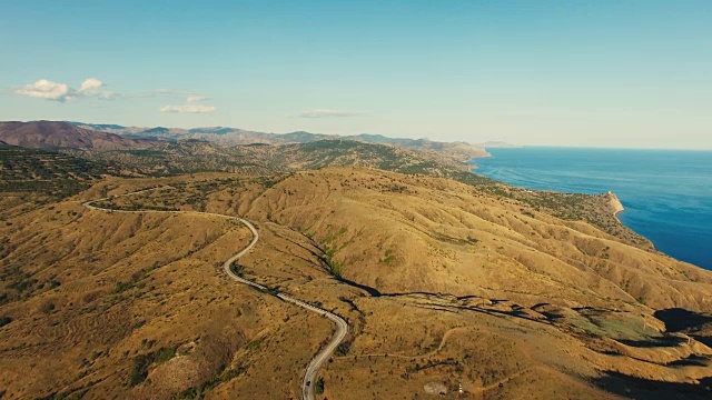 空中:高速公路穿过丘陵地带，有遥远的山脉和蓝色的海洋视频素材