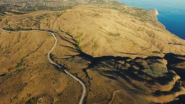 空中:高速公路穿过丘陵地带，有遥远的山脉和蓝色的海洋视频素材