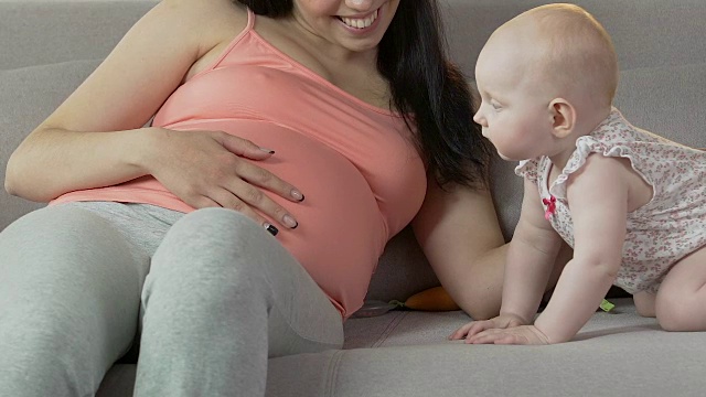 婴儿四肢着地站在沙发上，看着孕妇揉肚子视频素材画面3
