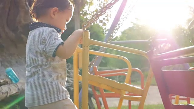 可爱的亚洲小男孩有乐趣推动秋千在操场上耀光在日落时间在慢动作视频素材