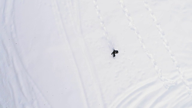 从空中俯瞰冬天穿着雪鞋在白雪覆盖的田野上行走的人。欧洲阿尔卑斯山户外自然景观雪山。4k无人机飞行直线向下的视角视频素材画面1