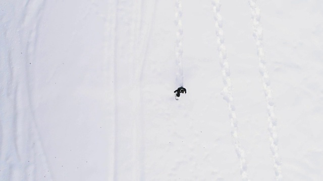 从空中俯瞰冬天穿着雪鞋在白雪覆盖的田野上行走的人。欧洲阿尔卑斯山户外自然景观雪山。4k无人机飞行直线向下的视角视频素材画面3