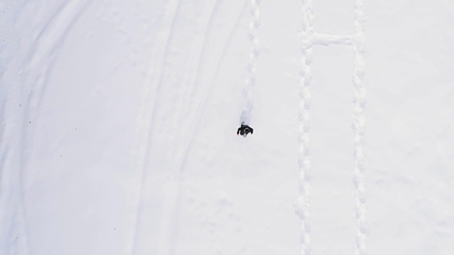 从空中俯瞰冬天穿着雪鞋在白雪覆盖的田野上行走的人。欧洲阿尔卑斯山户外自然景观雪山。4k无人机飞行直线向下的视角视频素材画面4