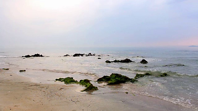 早晨的阳光与海洋，柔软的波浪和岩石在海上，绿色苔藓在热带海滩的沙子。视频素材