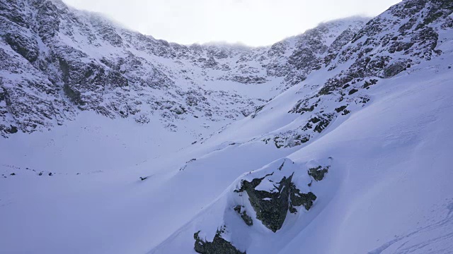 在寒冷的阳光明媚的天气里，滑雪游览覆盖在雪中的岩石山脉景观视频素材