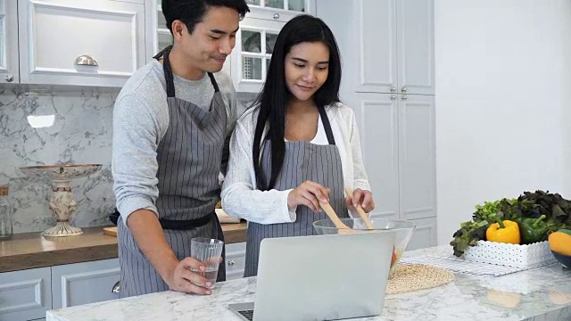 年轻夫妇在厨房做饭时使用笔记本电脑视频素材