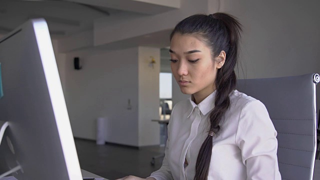 肖像美丽的商业女人是工作，坐在桌子与电脑在金融公司，看着显示器，打字文本，触摸脸。FullHD视频素材画面2