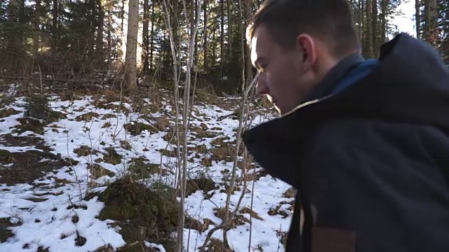 在阳光明媚的日子里，年轻的徒步旅行者背着背包走在山间的松林里。他在早春徒步旅行。美丽的风景作为背景。特写慢动作视频素材