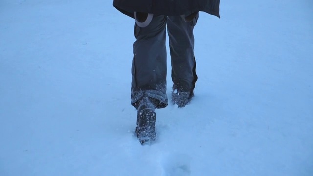 后视图的男性的脚走过在晚上的雪地在田野。一个面目全非的家伙在冬季旅行中享受自由。假期的概念。特写慢动作视频素材