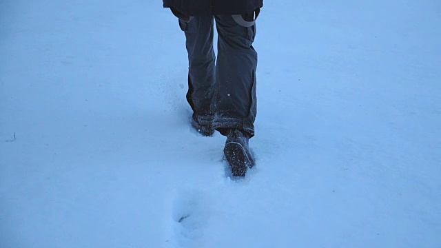 后视图的男性的脚走过在晚上的雪地在田野。一个面目全非的家伙在冬季旅行中享受自由。假期的概念。特写慢动作视频素材