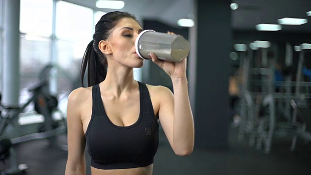 健身女性锻炼后喝蛋白质奶昔，肌肉获得营养，健康视频素材画面1