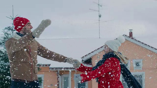 年轻美丽的夫妇在飘落的雪中跳舞和旋转。快乐的男人和女人在他们田园诗般的房子的院子里玩耍。家庭享受冬天。视频素材