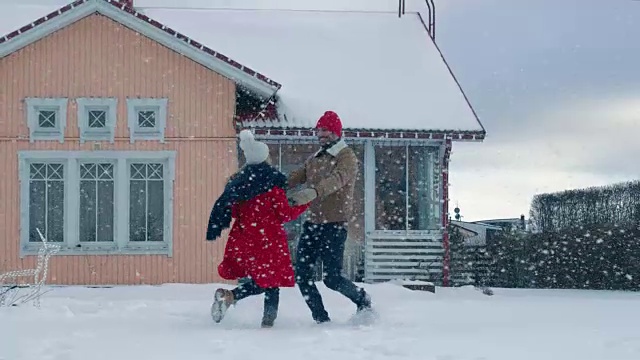 年轻美丽的夫妇在飘落的雪中跳舞和旋转。快乐的男人和女人在他们田园诗般的房子的院子里玩耍。视频素材