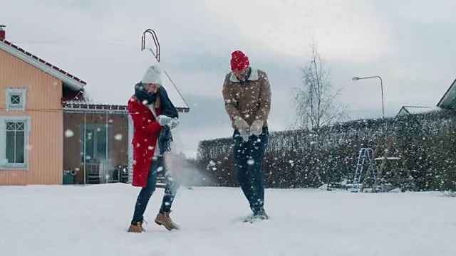 年轻美丽的夫妇互相扔雪球当雪落下。快乐的男人和女人在他们田园诗般的房子的院子里玩雪。家庭享受冬天。视频素材