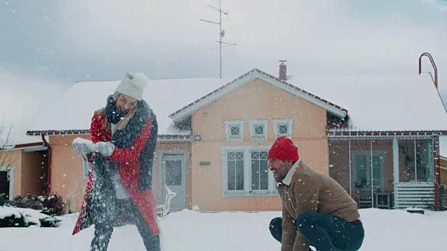 年轻美丽的夫妇互相扔雪球当雪落下。快乐的男人和女人在他们田园诗般的房子的院子里玩雪。家庭享受冬天。视频素材