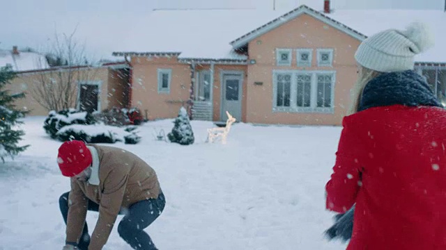 年轻美丽的夫妇互相扔雪球当雪落下。快乐的男人和女人在他们田园诗般的房子的院子里玩雪。家庭享受冬天。视频素材