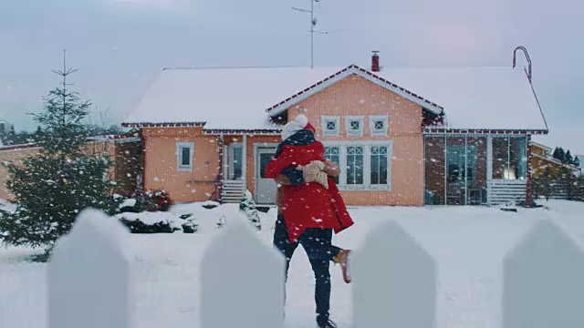 年轻美丽的夫妇跑出房子到院子里覆盖着新雪，他们旋转和跳舞。快乐的年轻人在神奇的冬天时间。视频素材