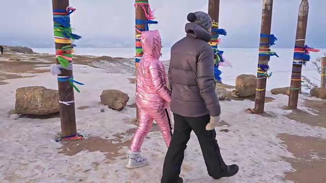 一对年轻夫妇喜欢在冬季的山顶户外散步。在贝加尔湖的圣地，冬天的佛教仪式柱子上系着彩带。视频素材画面2