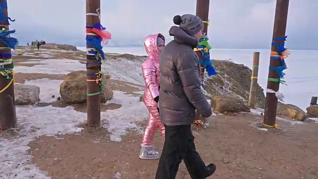 一对年轻夫妇喜欢在冬季的山顶户外散步。在贝加尔湖的圣地，冬天的佛教仪式柱子上系着彩带。视频素材画面3