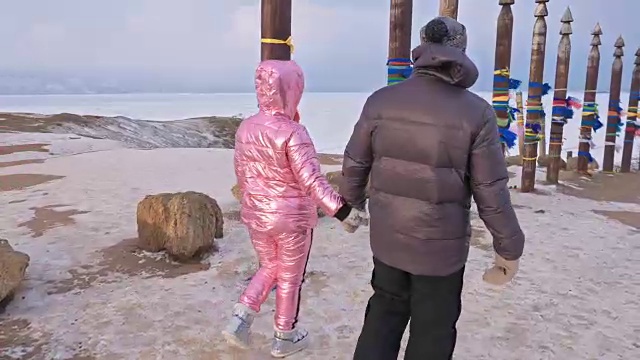 一对年轻夫妇喜欢在冬季的山顶户外散步。在贝加尔湖的圣地，冬天的佛教仪式柱子上系着彩带。视频素材画面4